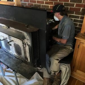 CSIA Certified Chimney Sweep in Virginia Beach cleaning a fireplace flue for a wood stove insert using rotary brush equipment.
